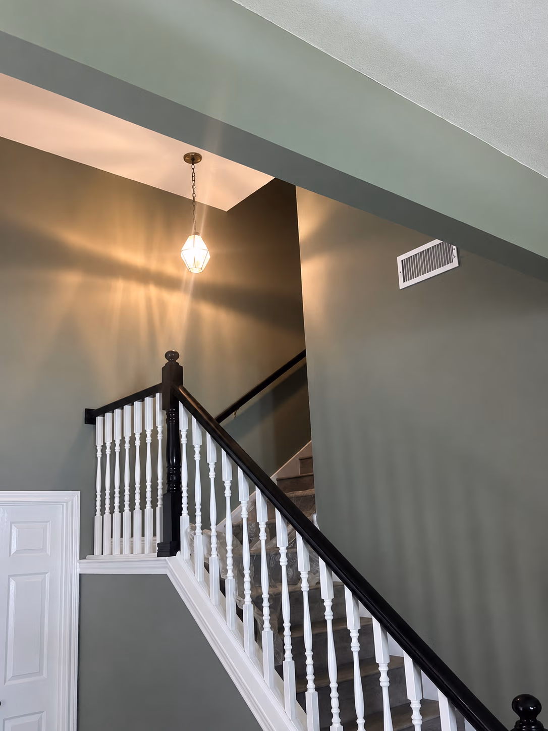 Indoor staircase with black banister, white spindles, gray carpet, green walls, and hanging light fixture.