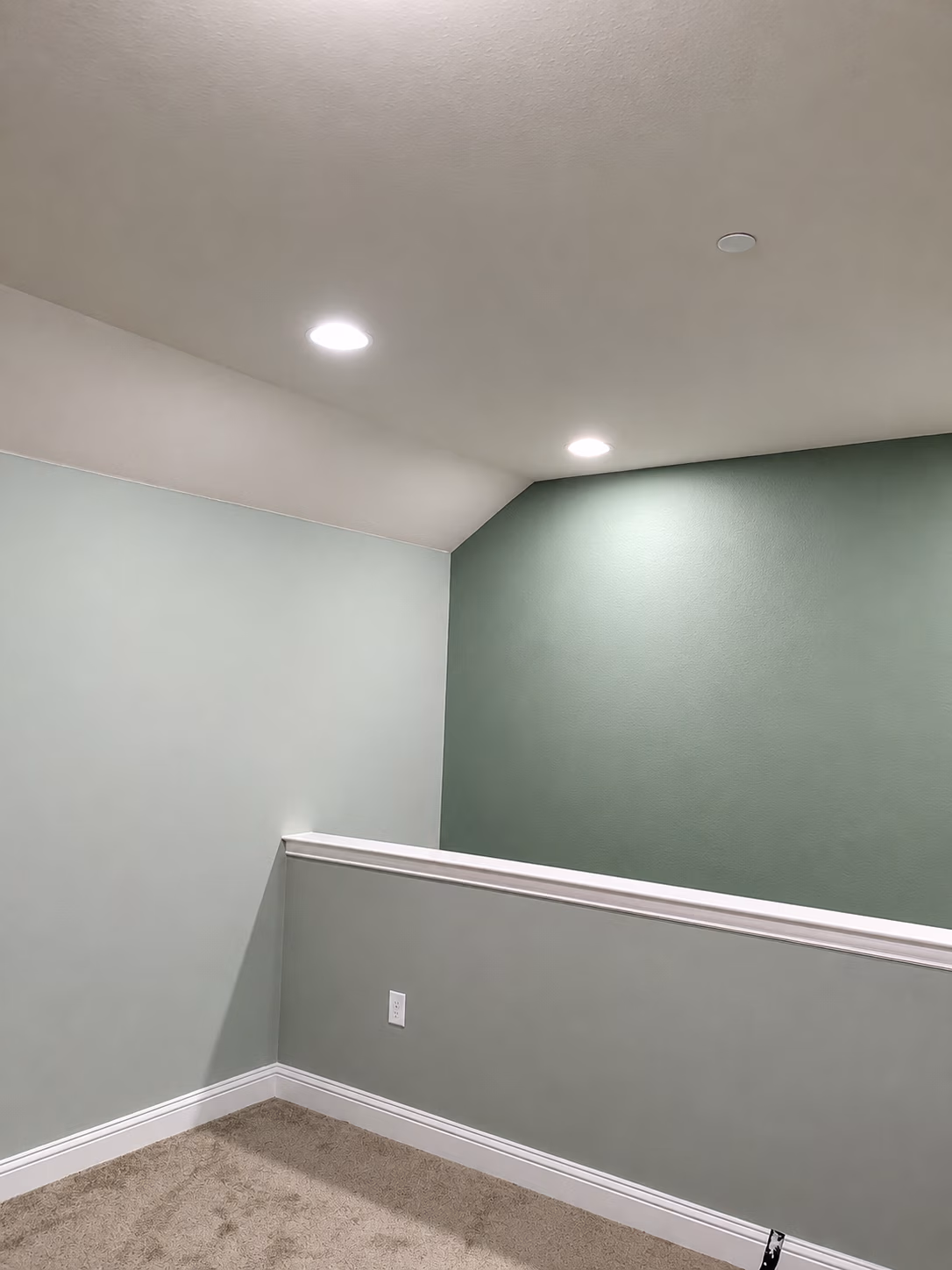 Interior corner with light green walls, beige carpet, white baseboard, and two ceiling lights.
