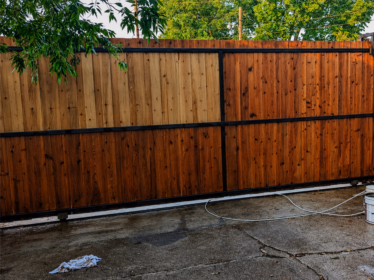 Wooden fence with two-tone staining and black metal frame on a cracked concrete ground.